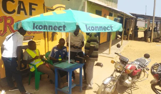 People using a Konnect Wi-Fi Hotspot sitting or standing under a large Konnect umbrella at a partner's site